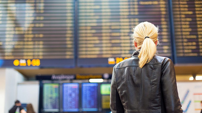 Woman at an airport looking up at the flight timetable.